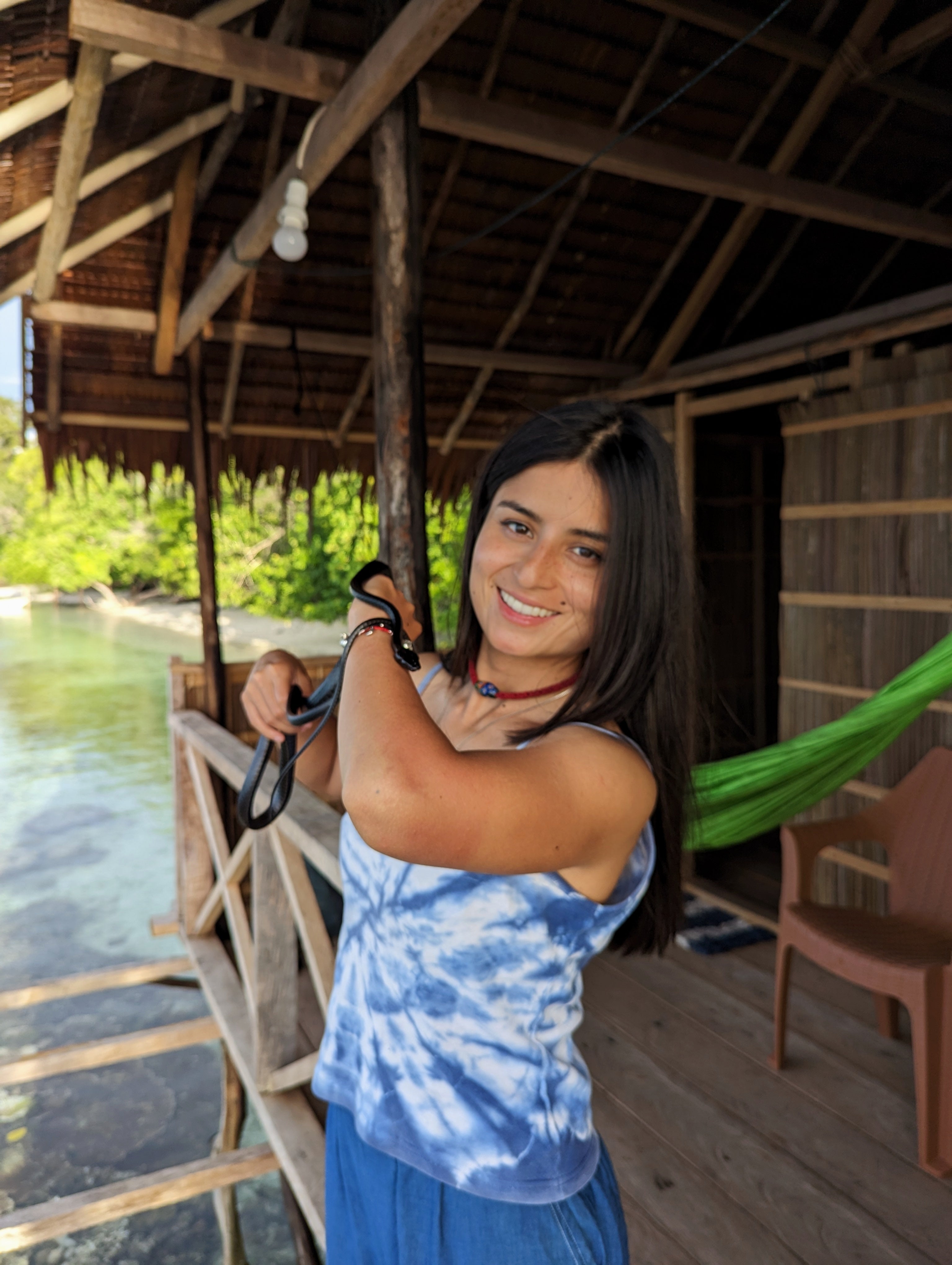 Majo holding a snake in a tropical hut